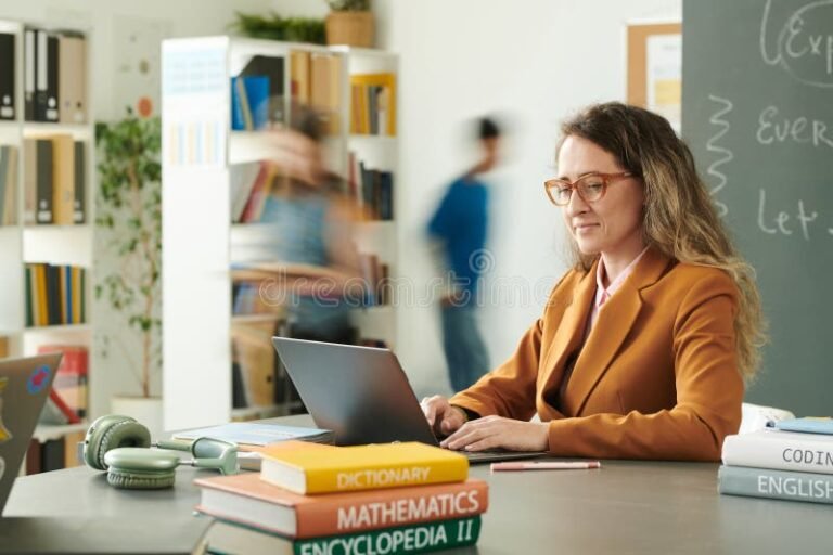 docente sonriendo con libros y computadora
